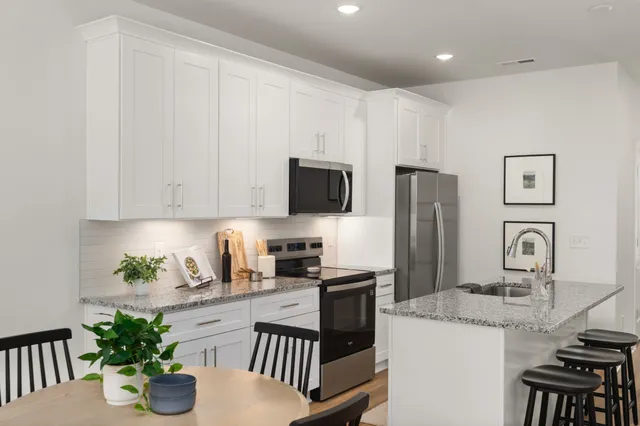 a kitchen with stainless steel appliances granite countertop a refrigerator a stove a sink dishwasher and white cabinets with wooden floor