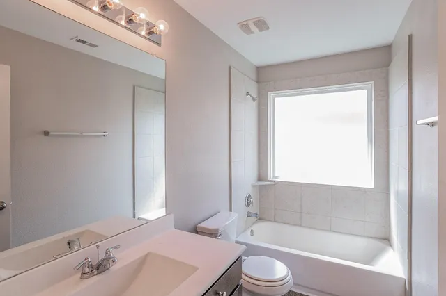 a bathroom with a bathtub shower sink vanity mirror and toilet