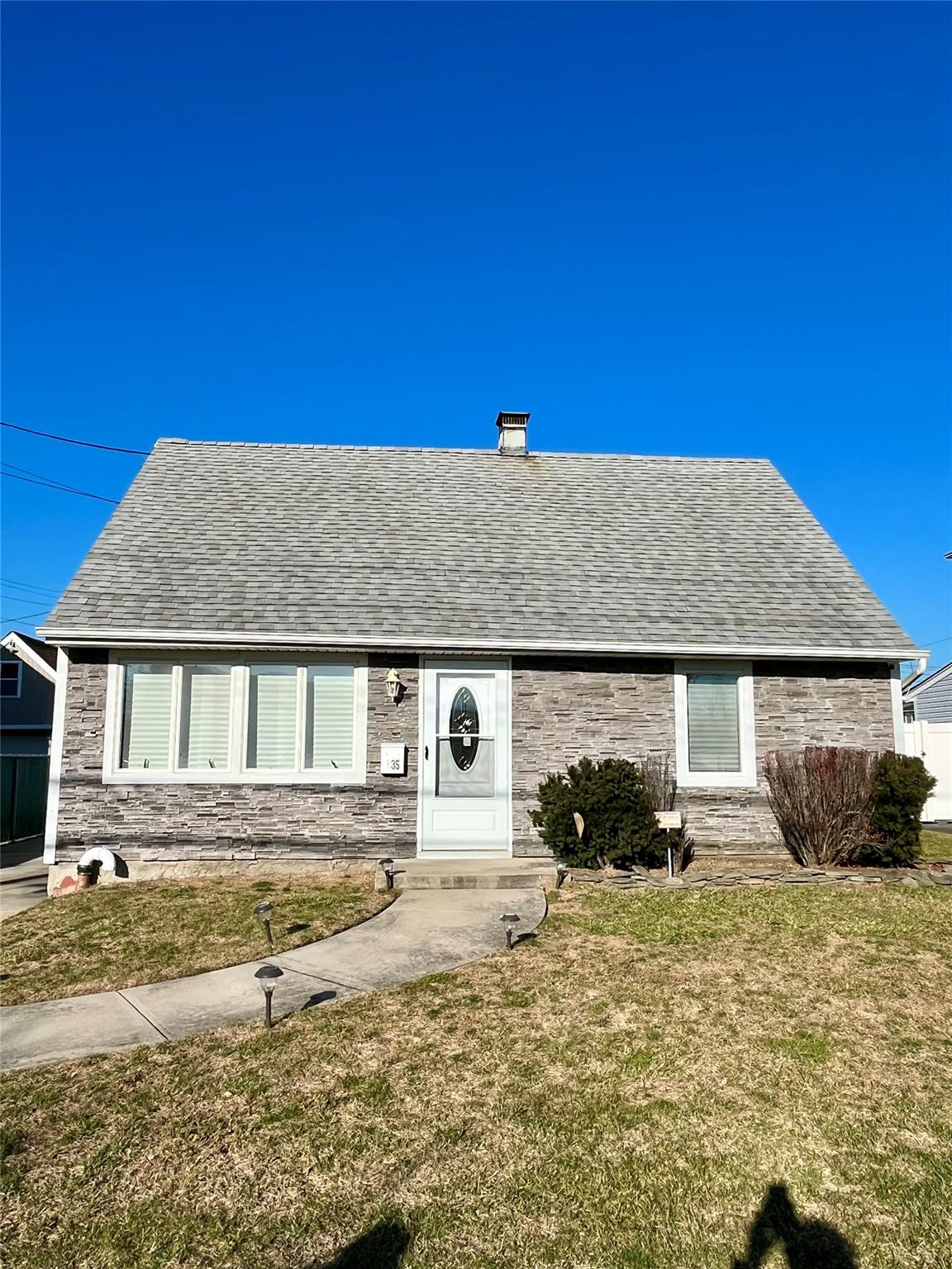 635 Barnes Avenue Baldwin, NY 11510 - Photo 1 of 1 View of front facade featuring a shingled roof, entry steps, a front lawn, and stone siding