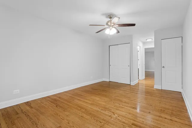 a view of an empty room with wooden floor and a ceiling fan