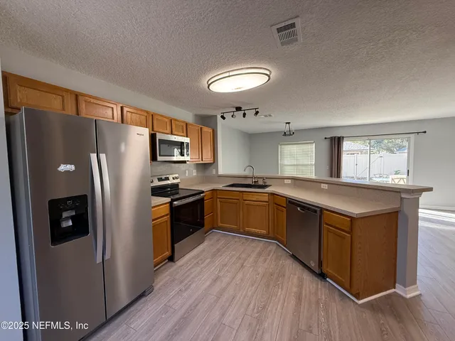 a large kitchen with stainless steel appliances granite countertop a sink dishwasher a stove and a refrigerator with wooden floor