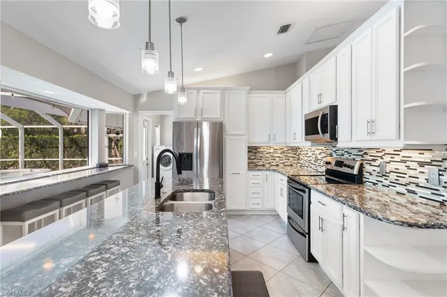 a kitchen with stainless steel appliances granite countertop a stove a sink dishwasher a refrigerator and a microwave oven with white cabinets