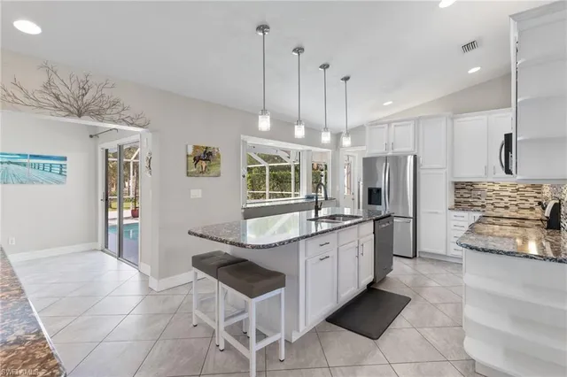 a kitchen with stainless steel appliances kitchen island granite countertop a sink a refrigerator a stove a microwave oven with white cabinets and wooden floor