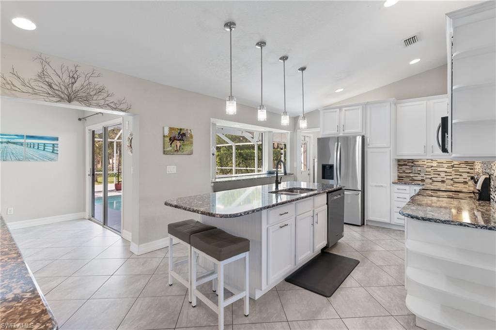 1061 15th Street Southwest Naples, FL 34117 - Photo 10 of 47 a kitchen with stainless steel appliances kitchen island granite countertop a sink a refrigerator a stove a microwave oven with white cabinets and wooden floor