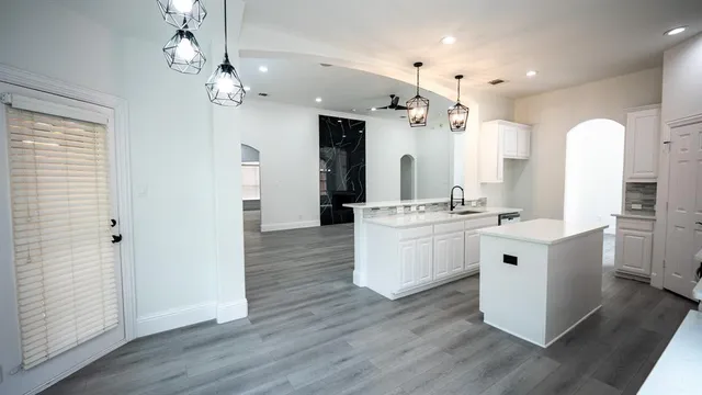 a large white kitchen with a white countertops a stove a sink and a large mirror with wooden floor