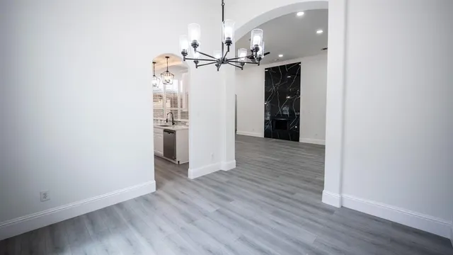an empty room with wooden floor staircase and kitchen view