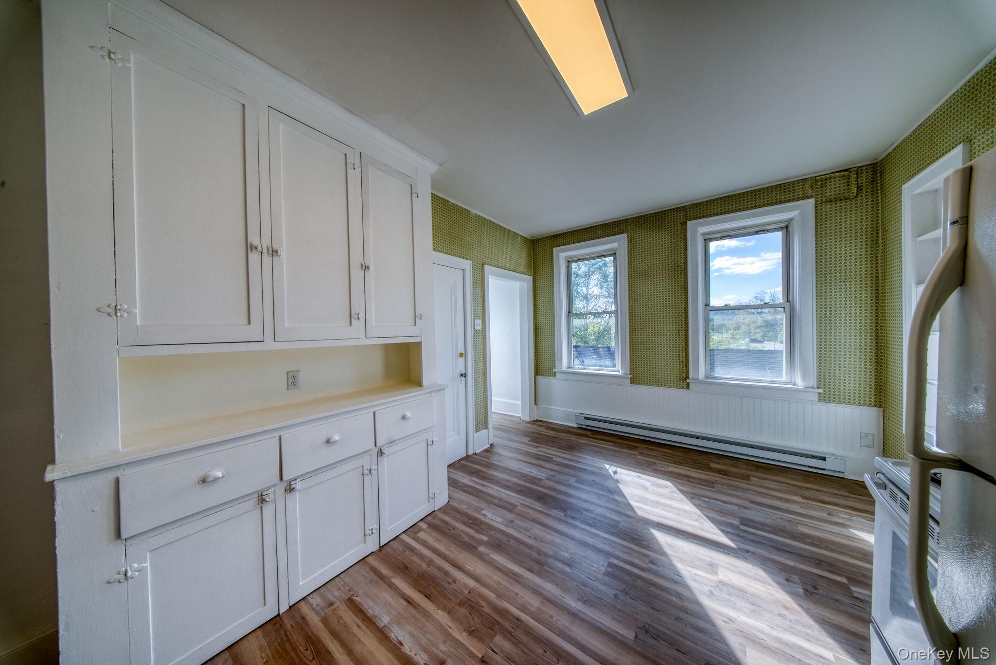 9 Mongaup Road Hurleyville, NY 12747 - Photo 6 of 35 Kitchen with white cabinetry, wallpapered walls, dark wood finished floors, baseboard heating, and white appliances