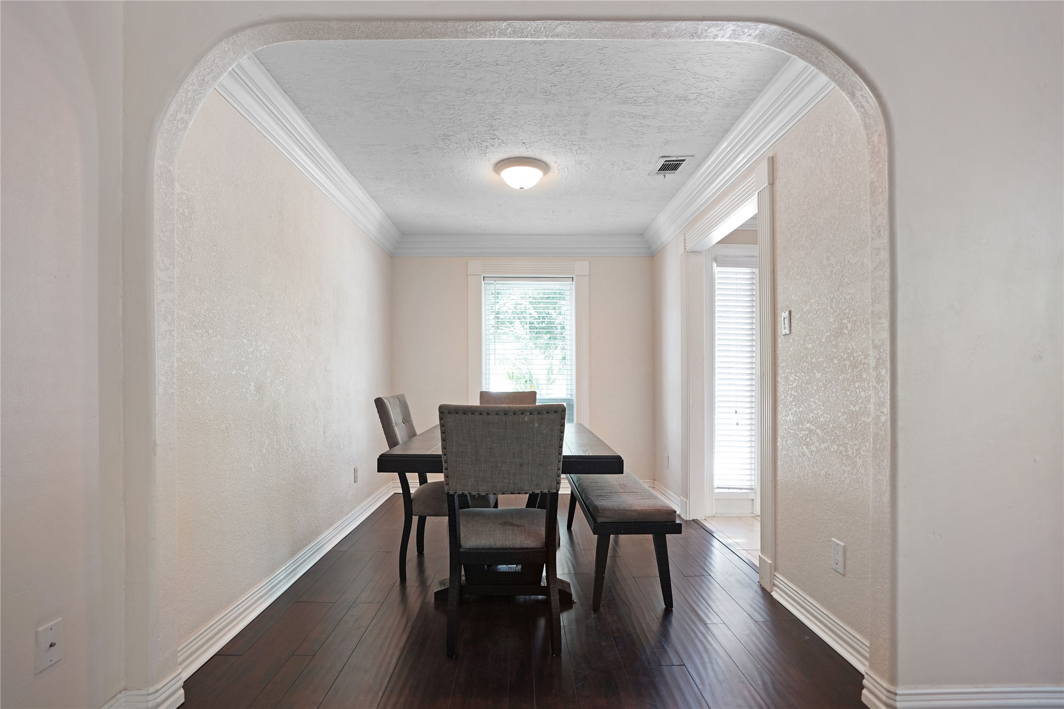 17119 Mellow Ridge Drive Spring, TX 77379 - Photo 14 of 32 This dining room features a cozy space with elegant archways, a large window providing natural light, and dark hardwood flooring. The room includes a modern dining set with seating and opens to an adjacent area through a doorway with vertical blinds.
