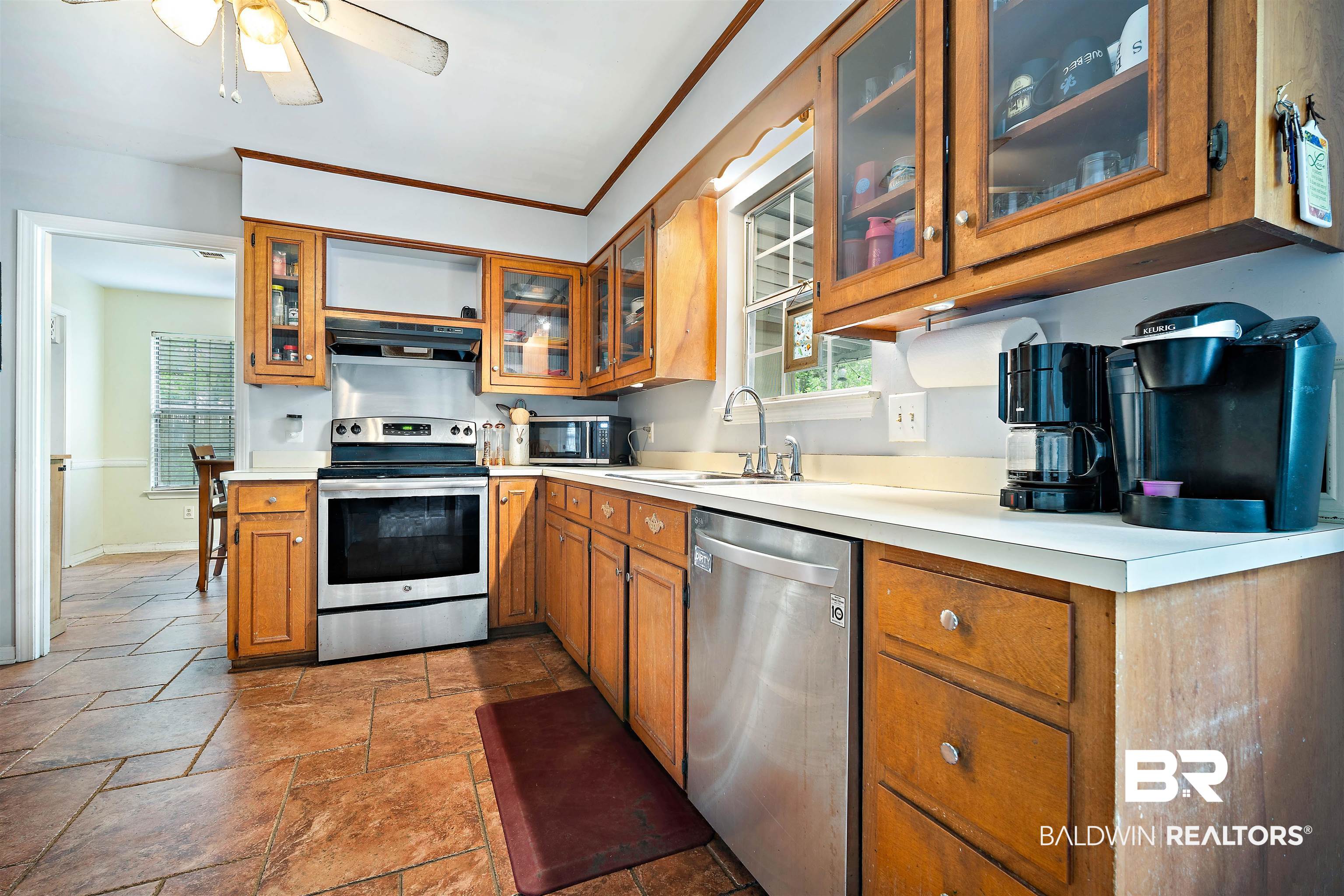 2823 Woodland Road Mobile, AL 36693 - Photo 7 of 29 Kitchen featuring a sink, stone tile floors, brown cabinetry, under cabinet range hood, and appliances with stainless steel finishes