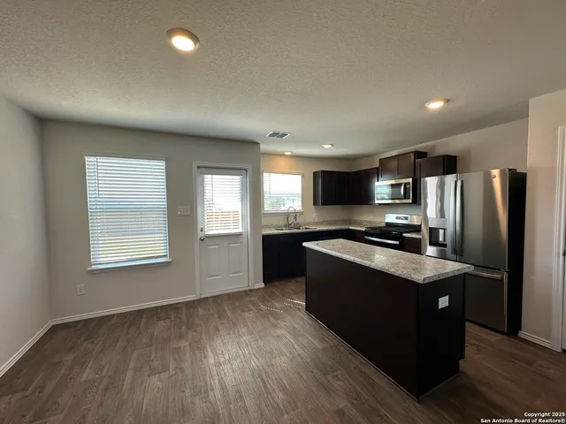 a kitchen with stainless steel appliances granite countertop a refrigerator a sink dishwasher a stove and white countertops with wooden floor