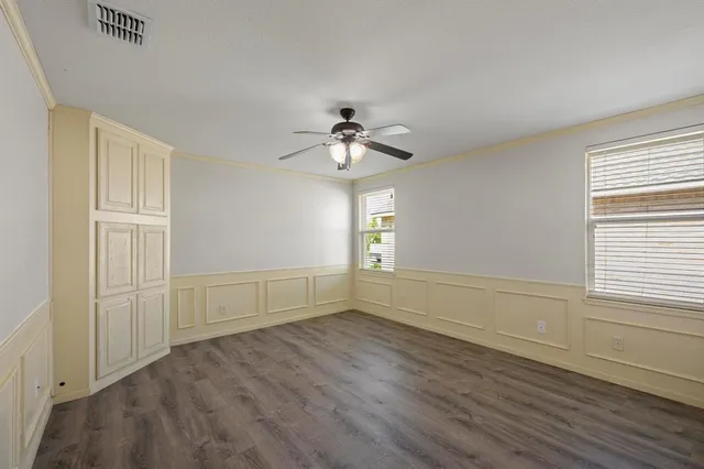 an empty room with wooden floor chandelier fan and windows