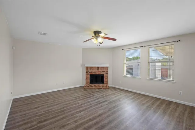 a view of an empty room with wooden floor fireplace and a window