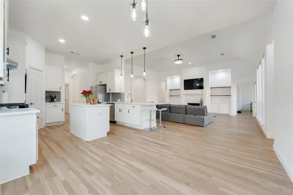 a large white kitchen with kitchen island a stove a sink dishwasher a refrigerator and white cabinets with wooden floor