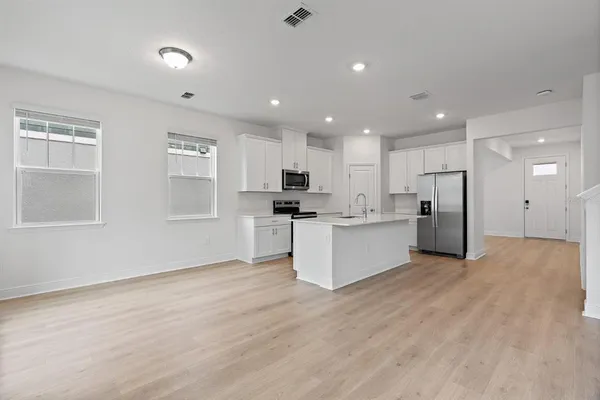 a view of kitchen with kitchen island stainless steel appliances refrigerator oven sink and white cabinets with wooden floor