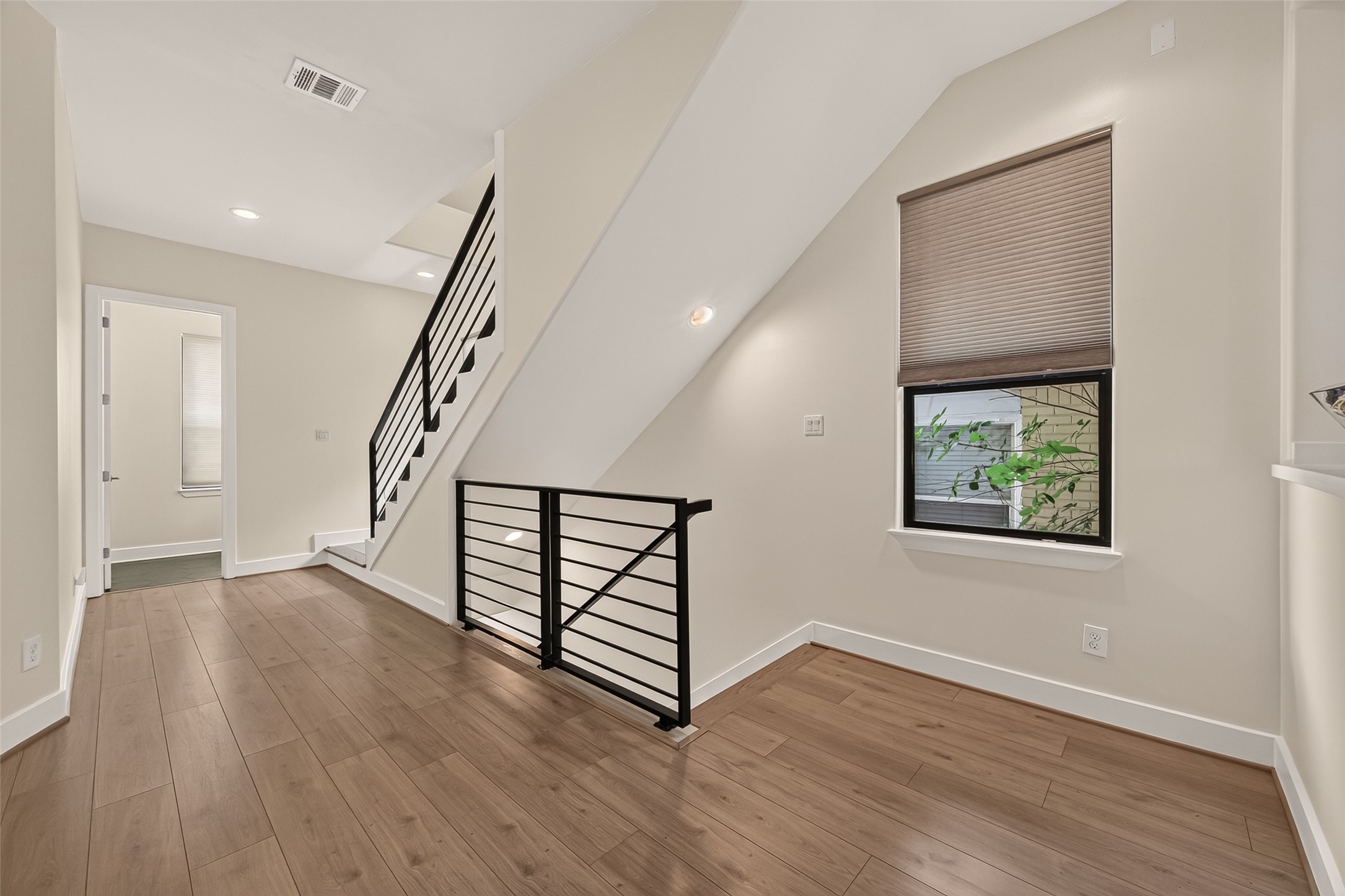 1767 Michigan Street Houston, TX 77006 - Photo 17 of 33 Bright and modern open space with light wood flooring, sleek black metal railings, and a staircase leading upwards. A window with a blind offers natural light, enhancing the clean and contemporary feel.