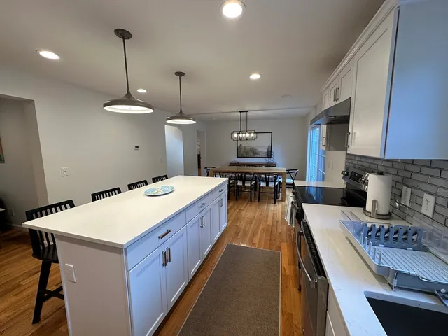 a large kitchen with a stove a sink dishwasher a oven a dining table and chairs with wooden floor