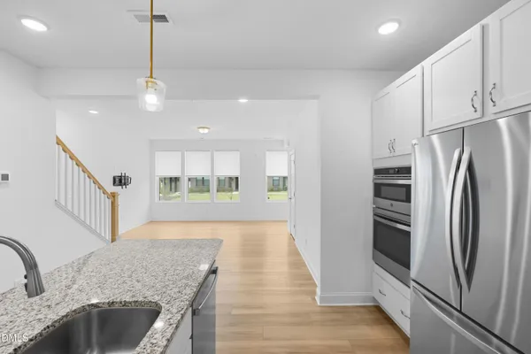 a kitchen with stainless steel appliances granite countertop a refrigerator a oven a sink dishwasher and white cabinets with wooden floor