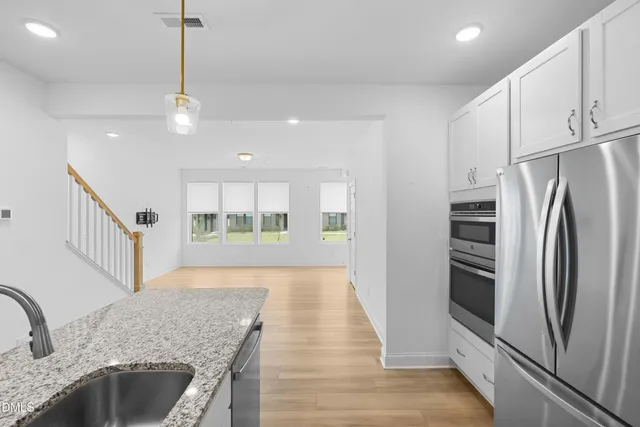 a kitchen with stainless steel appliances granite countertop a refrigerator a oven a sink dishwasher and white cabinets with wooden floor