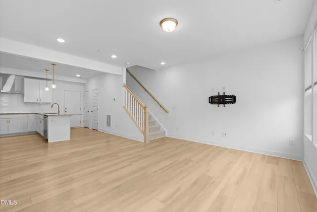 a view of an empty room with wooden floor and a kitchen