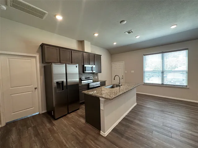 a kitchen with stainless steel appliances granite countertop a refrigerator a sink a stove and wooden floors