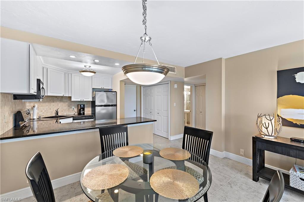 1 Bluebill Avenue, Unit 409 Naples, FL 34108 - Photo 7 of 17 a kitchen with stainless steel appliances granite countertop a sink a stove a dining table and chairs with wooden floor