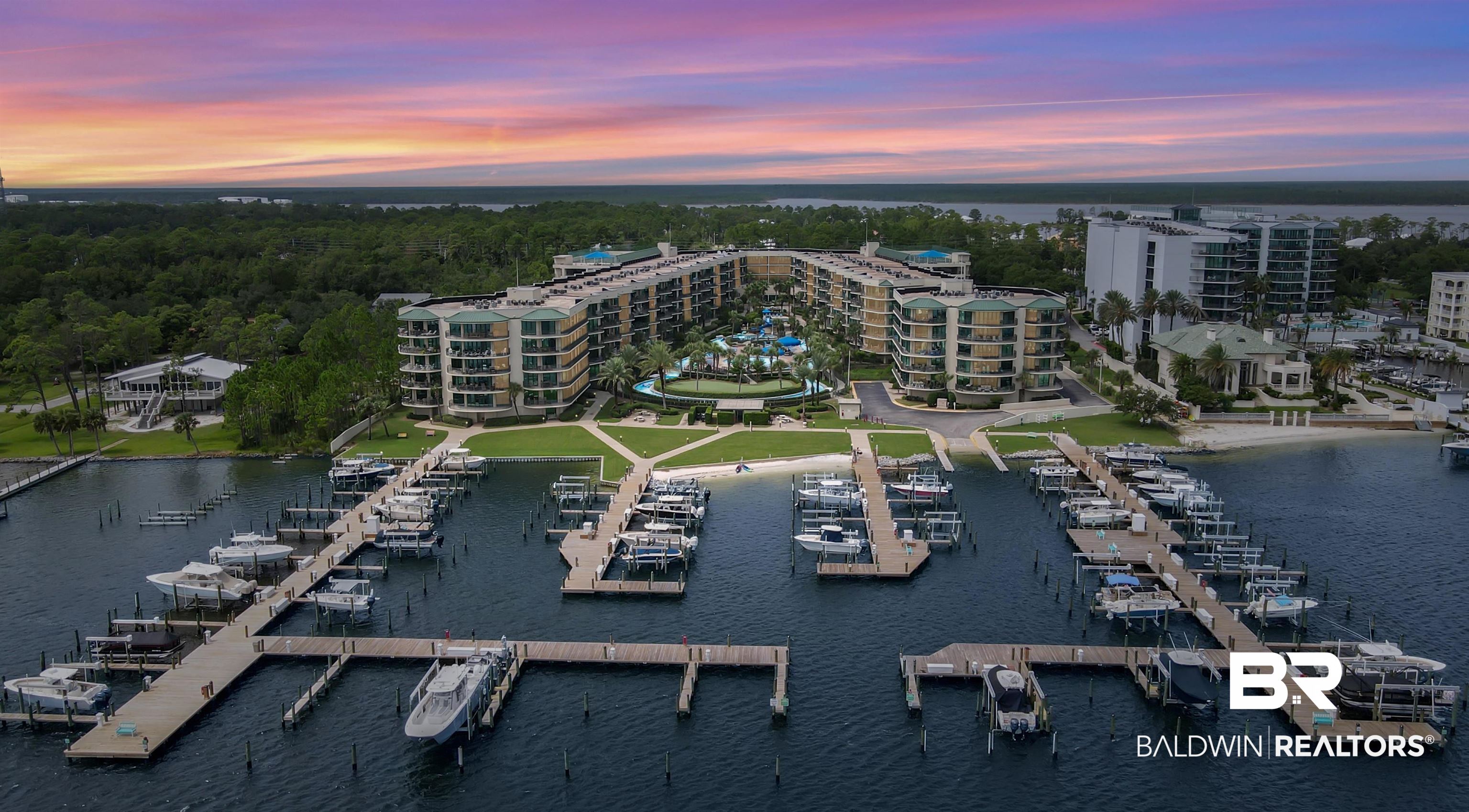 27580 Canal Road, Unit 1421 Orange Beach, AL 36561 - Photo 10 of 40 Expansive waterfront property featuring a private marina with multiple boat slips, a multi-story residential building with balconies, a manicured green space, and direct water access
