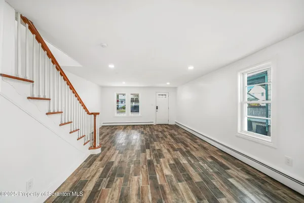 a view of an empty room with wooden floor and stairs