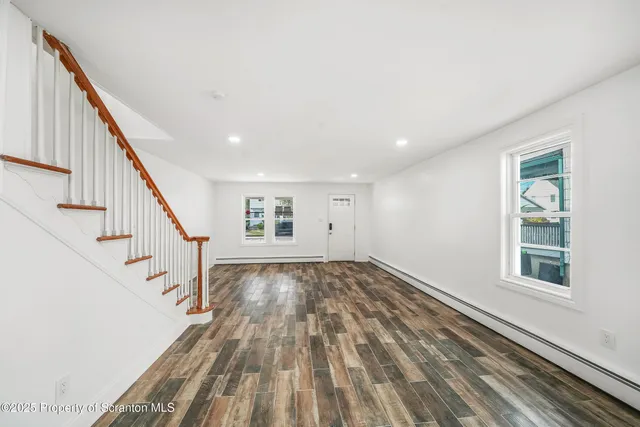 a view of an empty room with wooden floor and stairs