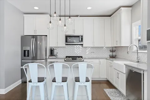 a kitchen with stainless steel appliances granite countertop white cabinets a sink a stove a refrigerator and island with wooden floor