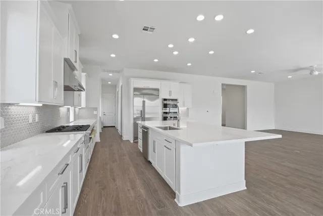 a large kitchen with stainless steel appliances granite countertop a large kitchen island a stove a sink a refrigerator and white cabinets with wooden floor