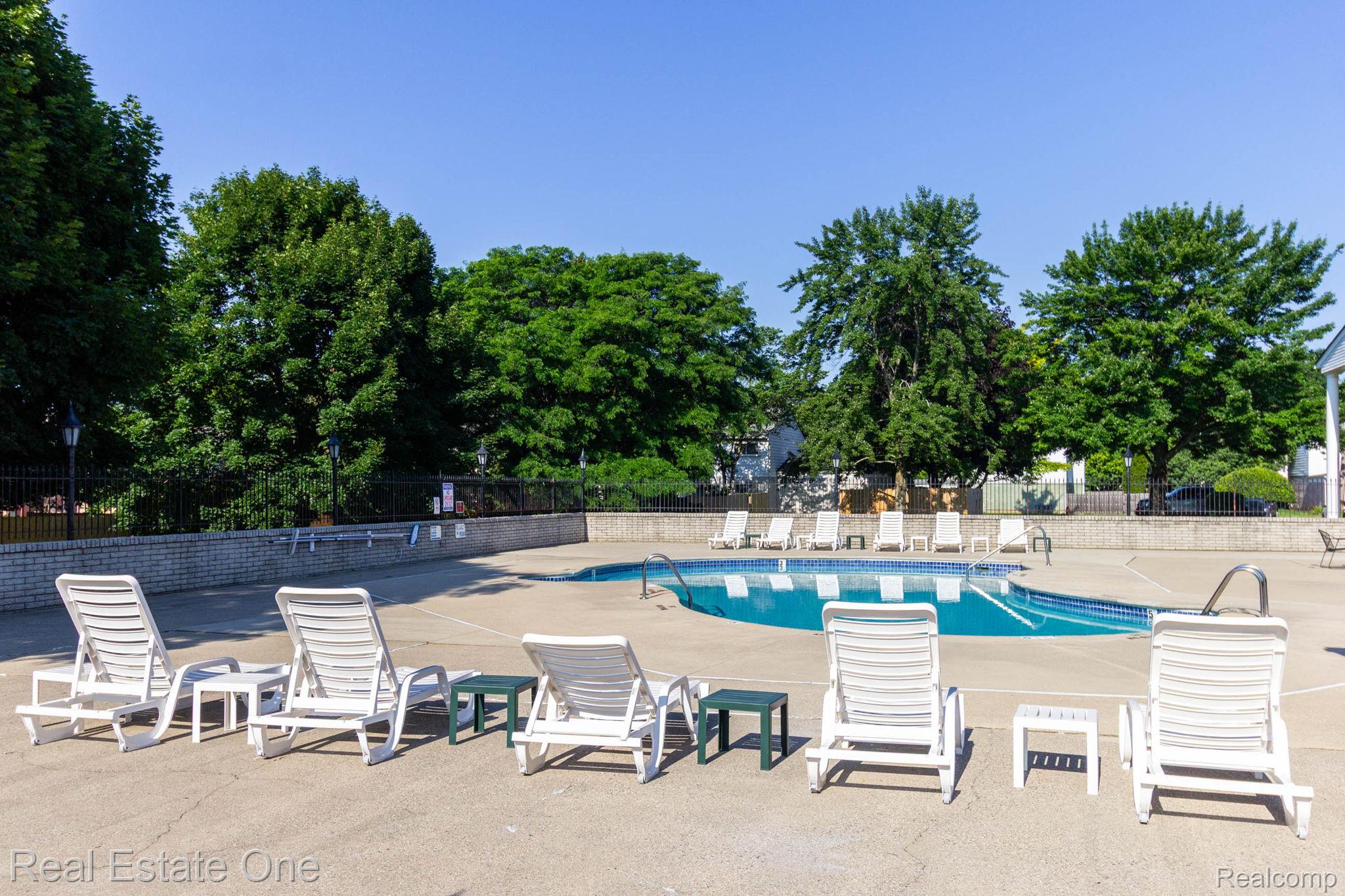 111 Manor Way Rochester, MI 48309 - Photo 34 of 36 Outdoor swimming pool with concrete decking, surrounded by mature trees, and a low brick wall