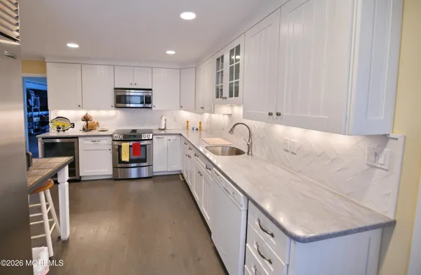 a kitchen with stainless steel appliances granite countertop a stove top oven a sink dishwasher and a refrigerator with wooden floor
