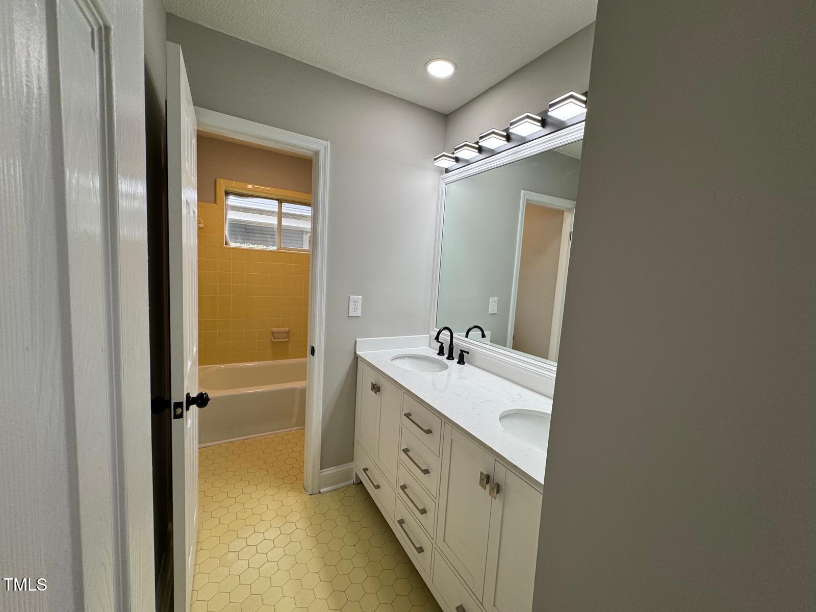 2616 Firelight Road Raleigh, NC 27610 - Photo 16 of 36 a bathroom with a double vanity sink a mirror and a bathtub