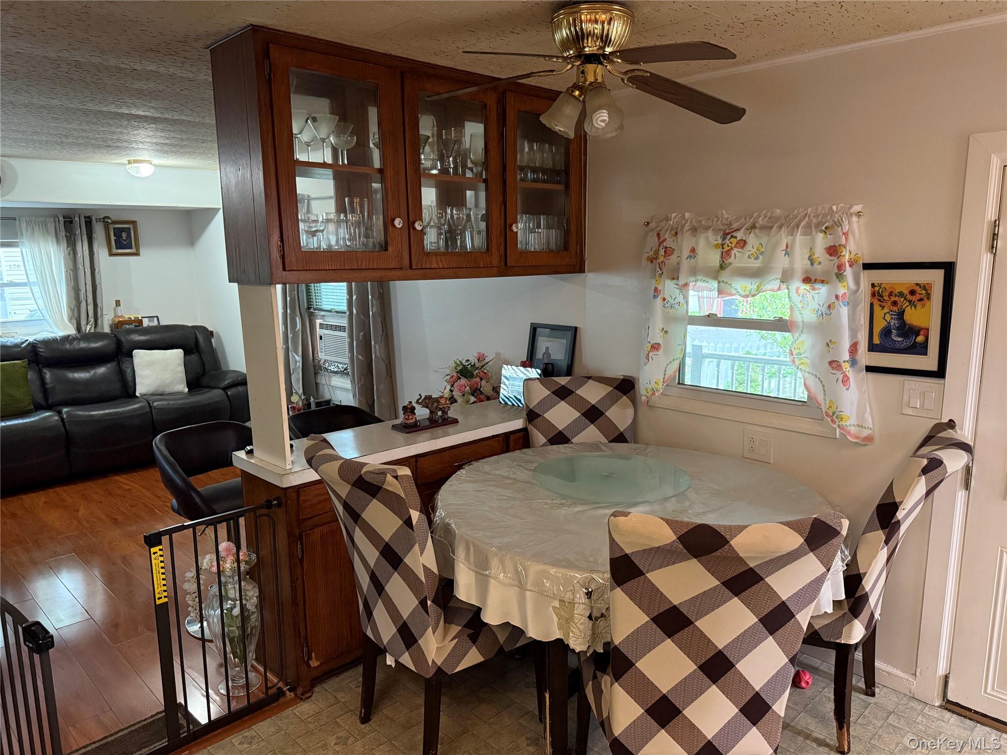 136 Quaker Rd Park Pomona, NY 10970 - Photo 10 of 24 Kitchen and living area featuring a built-in wood-finish cabinet with glass doors, a ceiling fan with integrated lighting, wood-finish flooring, a breakfast bar, and a window with natural light
