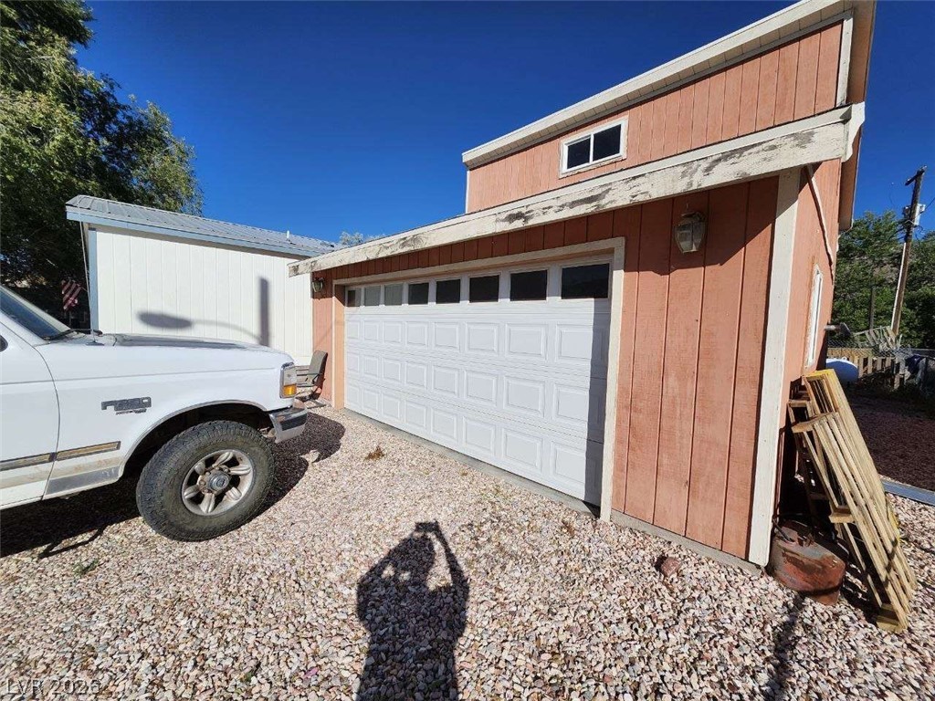 942 Holt Caliente, NV 89008 - Photo 6 of 22 A detached garage features a white door, contrasting with the reddish-brown siding and gravel driveway.