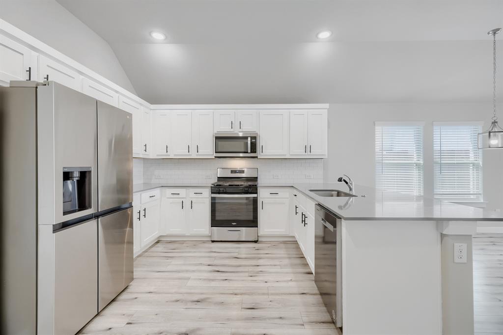 114 Mandarin Street Forney, TX 75126 - Photo 3 of 11 Modern kitchen featuring white shaker cabinetry, stainless steel appliances, light wood-finish flooring, a white subway tile backsplash, and a breakfast bar with a single basin sink