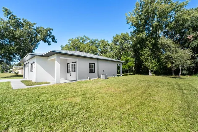 a yellow house with a big yard plants and large trees