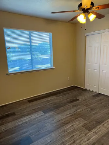 a view of an empty room with wooden floor and a fan