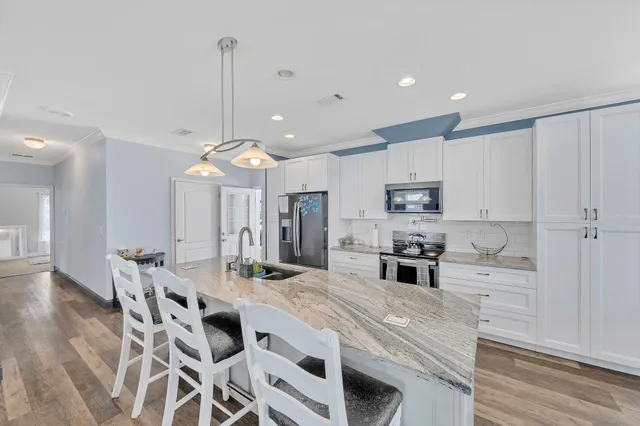 a kitchen with stainless steel appliances kitchen island granite countertop a sink a stove a refrigerator and island with wooden floor