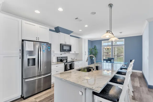 a kitchen with stainless steel appliances granite countertop a refrigerator a sink dishwasher a stove and a dining table with wooden floor