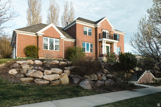 View of front of home with brick siding, roof with shingles, and a balcony