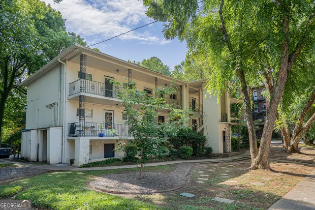 a view of a white house next to a yard with big trees