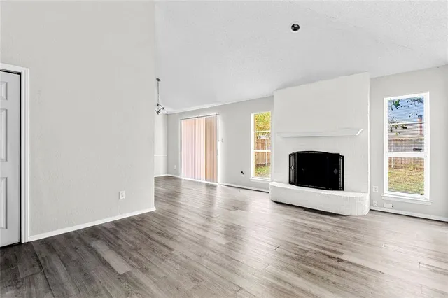 an empty room with wooden floor fireplace and windows