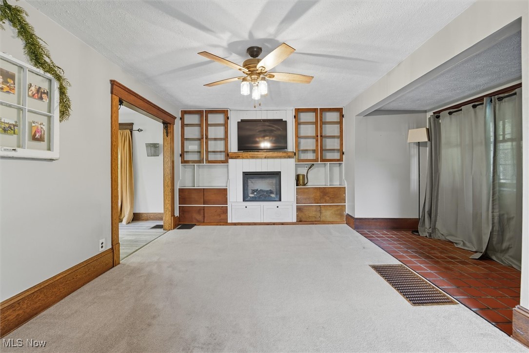 10536 Johnnycake Ridge Road Painesville, OH 44077 - Photo 13 of 40 Unfurnished living room featuring ceiling fan, a fireplace, a textured ceiling, and dark carpet