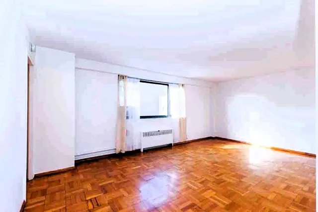 a view of an empty room with window and wooden floor