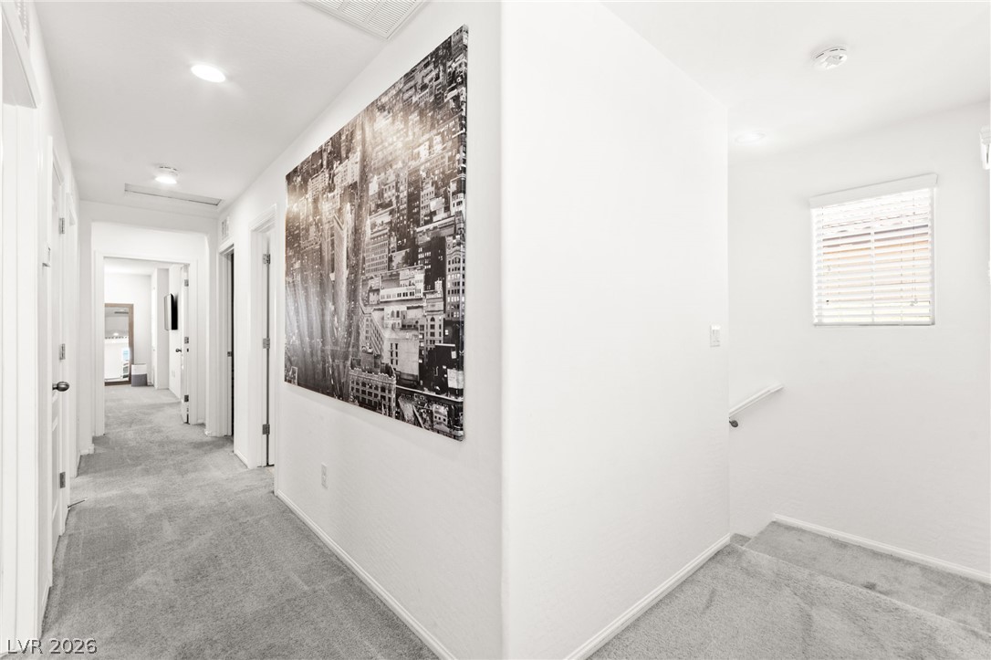 6435 Point Isabel Way Las Vegas, NV 89122 - Photo 23 of 57 A well-lit hallway with plush carpeting provides access to multiple rooms, illuminated by recessed lighting.