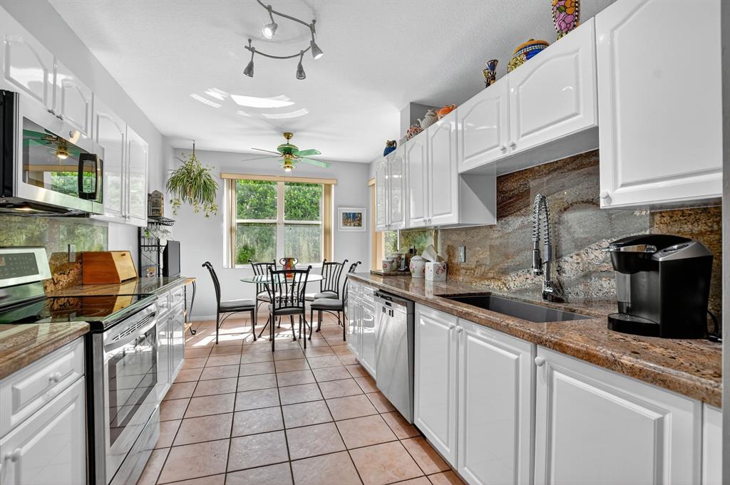 12614 Tiboli Chase Court, Unit 1 Boca Raton, FL 33496 - Photo 3 of 62 a kitchen with stainless steel appliances granite countertop a stove top oven a sink a dining table and chairs with white cabinets