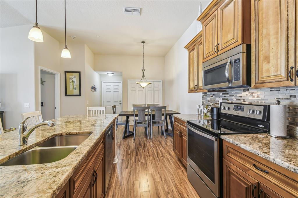 5088 Royal Palms Way, Unit 304 New Port Richey, FL 34652 - Photo 11 of 93 a kitchen with granite countertop a stove a sink a dining table and chairs with wooden floor
