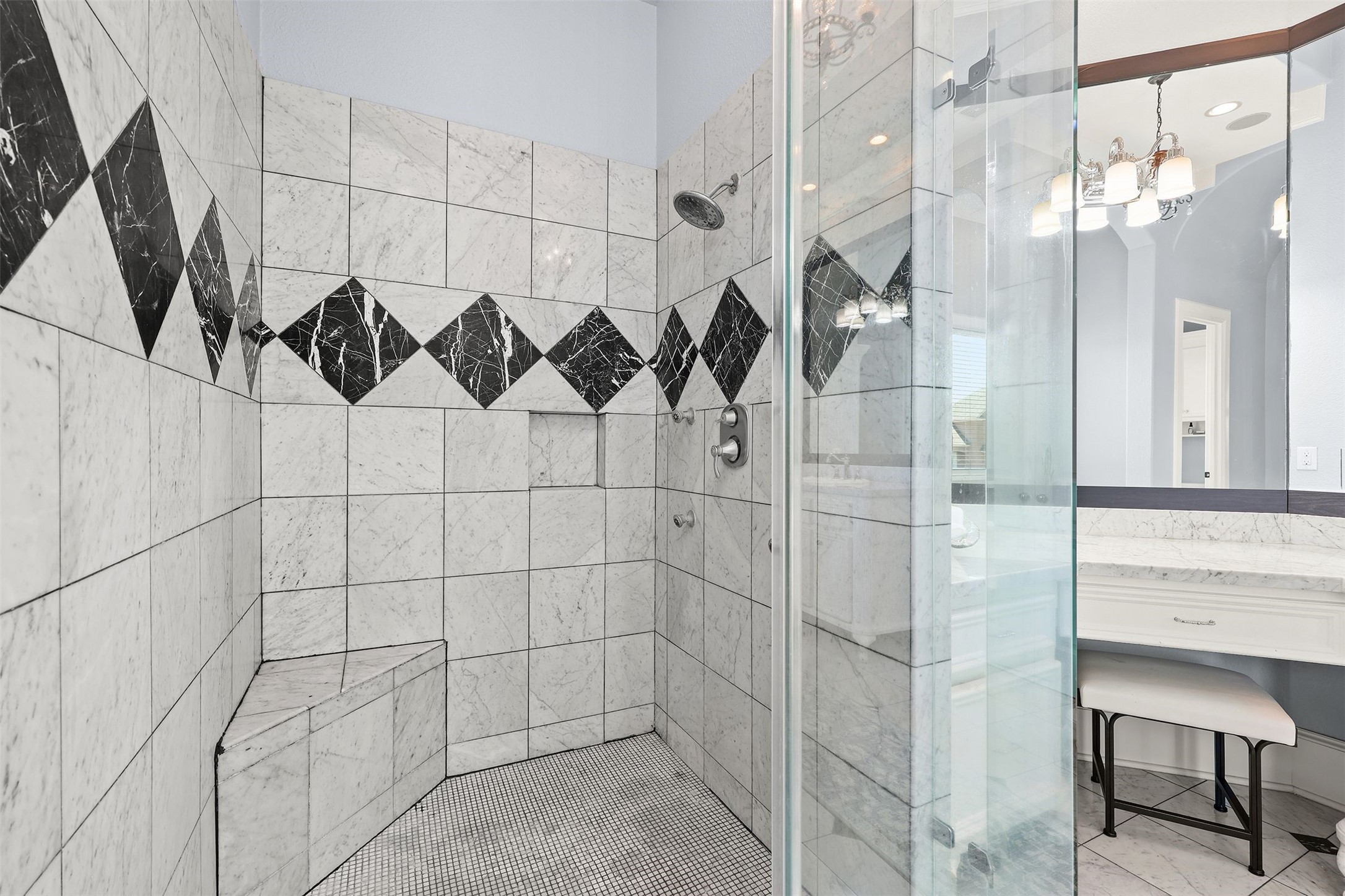 10896 Decatur Street Willis, TX 77318 - Photo 36 of 50 This modern bathroom boasts a glass-enclosed shower with elegant marble tiles and a striking black diamond pattern, complemented by a built-in bench, stylish lighting, and a spacious mirror for a bright, luxurious feel.