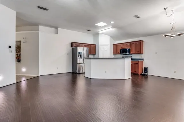 an empty room with wooden floor and a kitchen